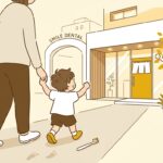 歯科医院の入口で保護者と手をつなぐ幼い子どもの後ろ姿と、そばに置かれた小さな歯ブラシ